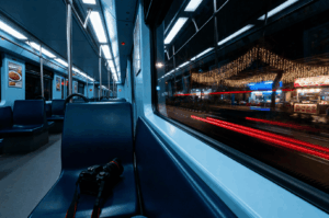 After-MRT- (1) Empty MRT car at night with a camera resting on a dark blue seat, contrasting the quiet interior with the glowing street outside, where festive lights and red vehicle trails hint at the city’s midnight energy—capturing the solitude and anticipation of a food photographer’s late-night journey.