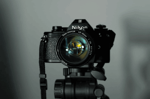 Night-And-Day- (1) Vintage Nikon film camera mounted on a tripod, spotlighted against a neutral gray backdrop—evoking the timeless precision behind both low-light and daylight food photography. The attached NIKKOR 50mm f/1.4 lens hints at cinematic depth and shallow focus, bridging analog artistry with modern visual storytelling.