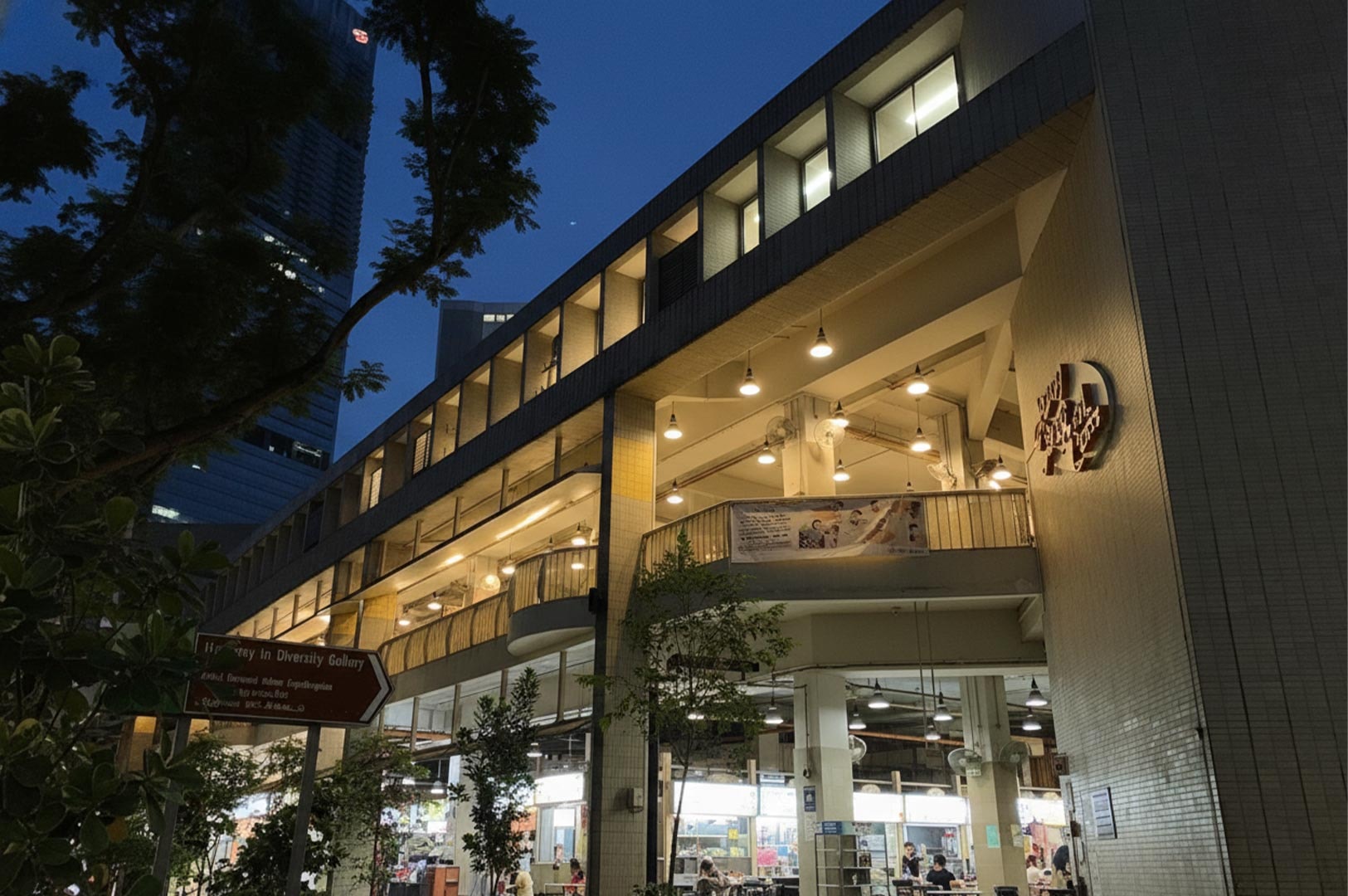 Exterior night view of the multi-story Amoy Street Food Centre in Singapore, featuring its distinct stepped-terrace architecture and illuminated open-air dining decks.