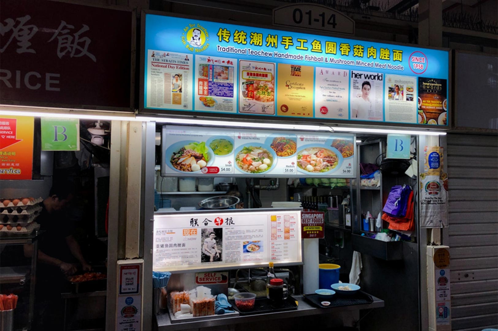Storefront of the famous Ah Ter Teochew Fishball Noodles hawker stall, displaying a blue signboard with menu items, newspaper clippings, and culinary awards.