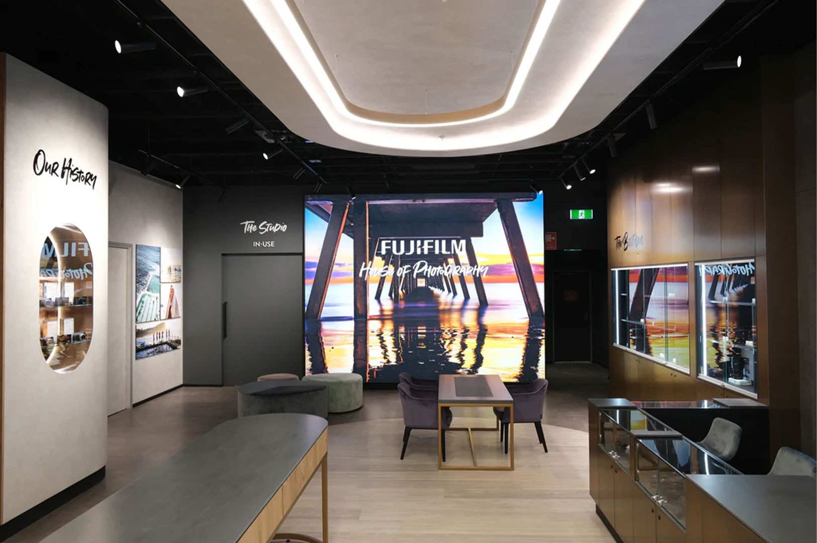 Interior design of the Fujifilm House of Photography showroom, featuring a large branding screen, sleek furniture, and glass display cases for cameras.