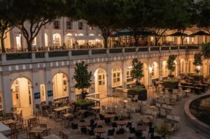 A wide night view of the historic CHIJMES courtyard in Singapore featuring illuminated neoclassical arches, outdoor restaurant seating, and lush trees.