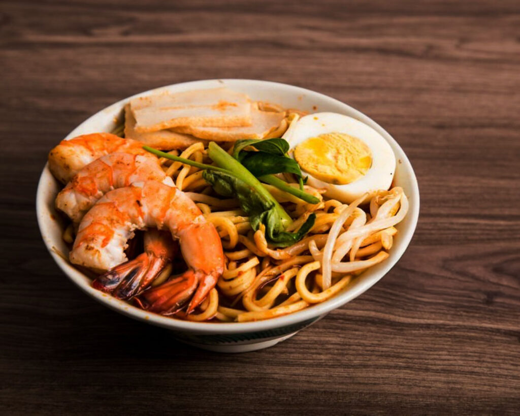 A close-up of a bowl of glossy, springy noodles topped with savoury sauce and garnishes, showing their firm texture and inviting shine under warm lighting.