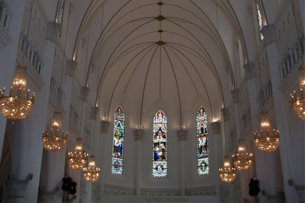 Interior view of CHIJMES Hall looking up at the high vaulted ceiling, ornate crystal chandeliers, and colorful arched stained glass windows.