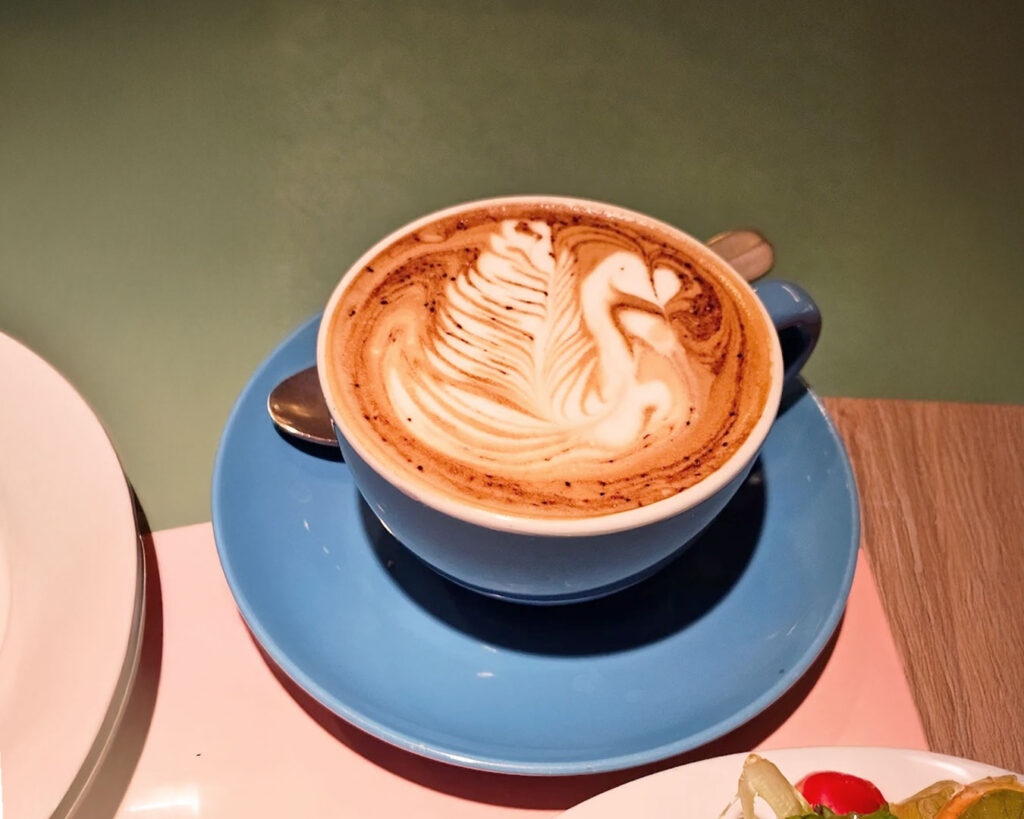 A cup of freshly brewed coffee served on a ceramic saucer at Marmalade Pantry, placed on a wooden table with soft café lighting and a relaxed dining setting in the background.