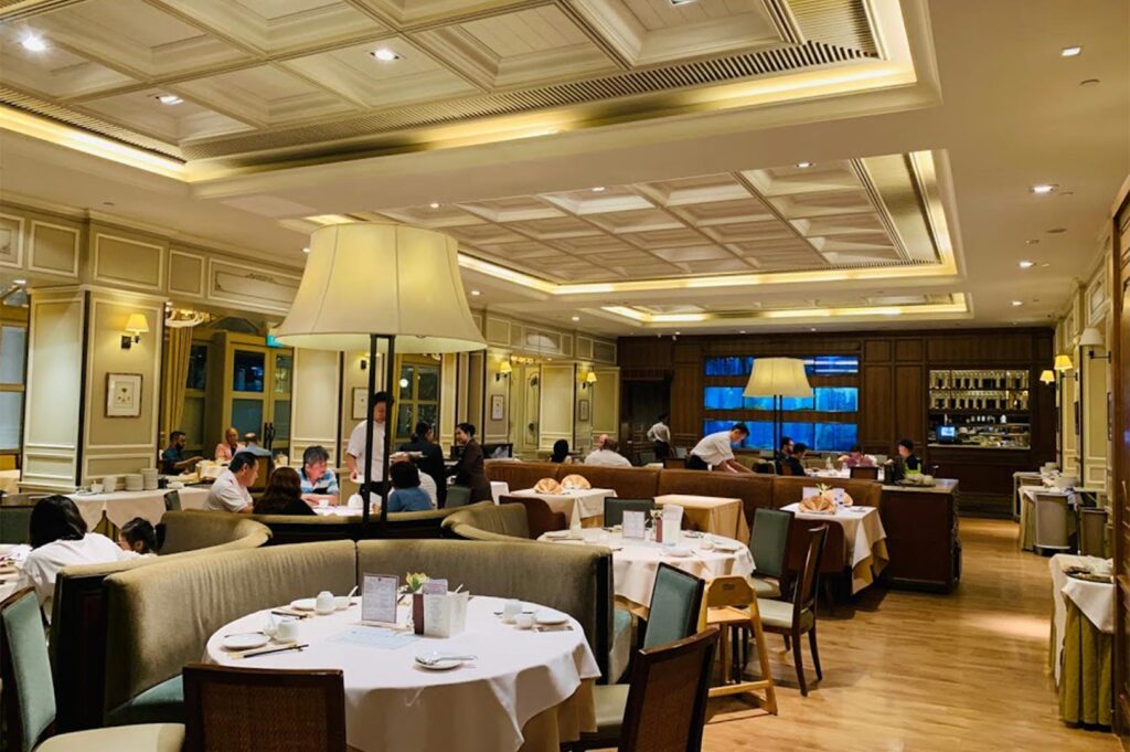 The elegant interior of a restaurant at CHIJMES, featuring classic wood paneling, coffered ceilings, and guests dining at round tables with white linens.