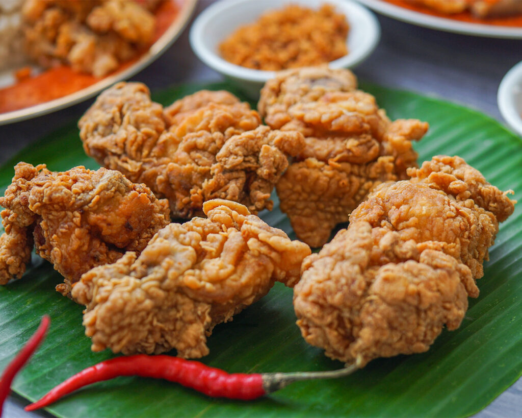 A close-up of crispy golden fried chicken served on a plate, showing textured crunchy batter and juicy meat inside, presented as a freshly cooked comfort food dish.