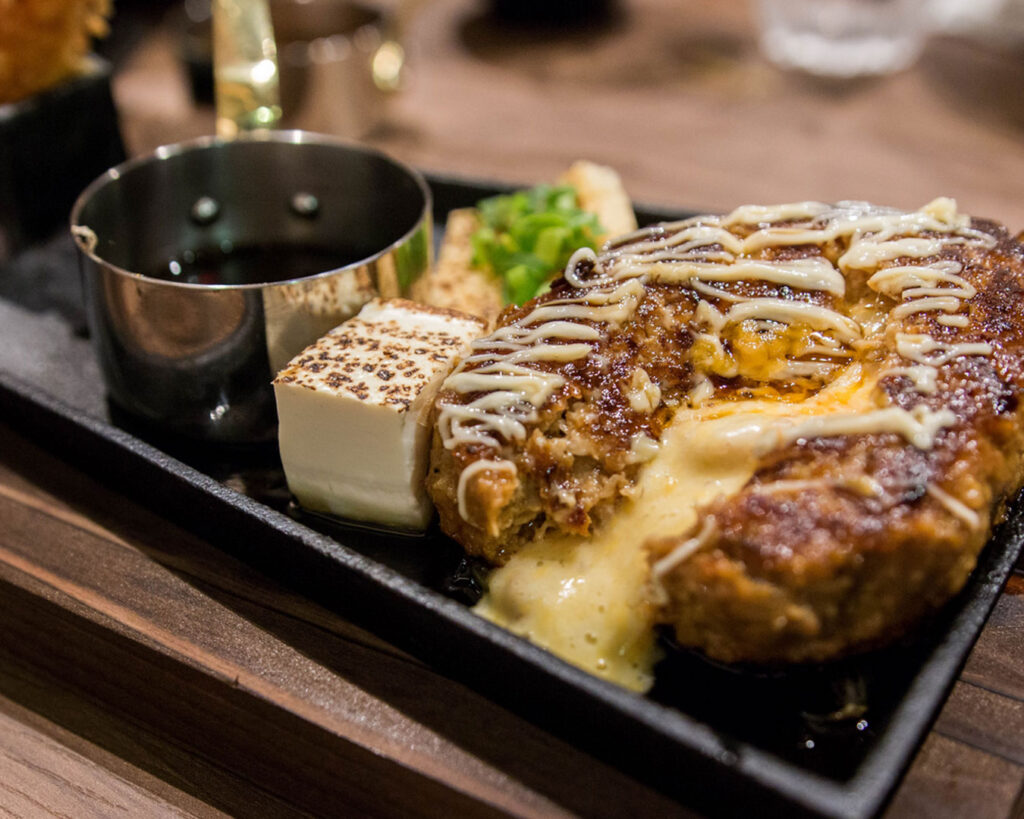A sizzling hamburg steak set from Hamburg Steak Keisuke served on a hot plate, accompanied by rice and side dishes, with steam rising to highlight the freshly cooked Japanese-style hamburger steak.