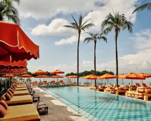 A relaxing scene at Tanjong Beach Club showing a sun lounger under a large white umbrella by the swimming pool, perfect for lounging under the sun.