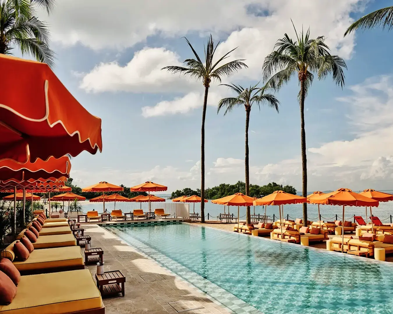 A relaxing scene at Tanjong Beach Club showing a sun lounger under a large white umbrella by the swimming pool, perfect for lounging under the sun.