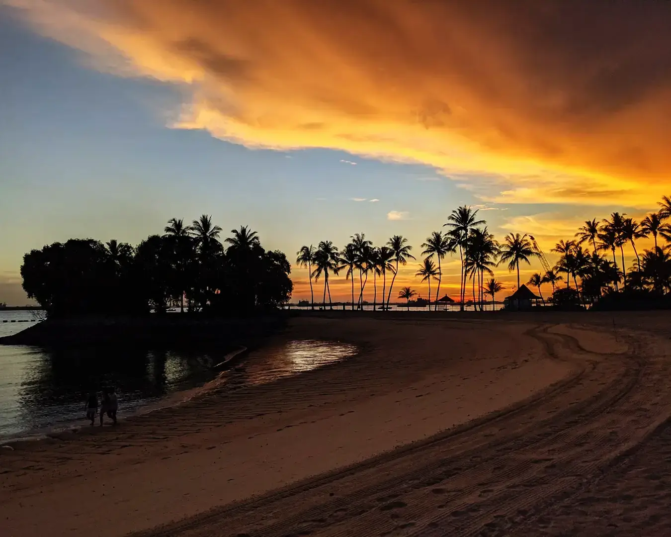 Nightfall at Tanjong Beach Club during sunset, showcasing soft lights along the beach and silhouetted palm trees against a colourful sky.