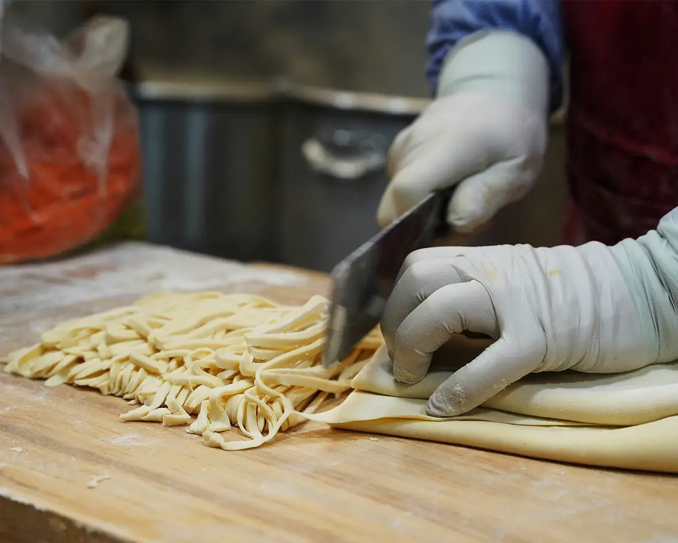 A close-up of hands skillfully cutting fresh dough into thin noodles, showing the texture and precision of the process, with flour lightly dusted across the work surface.