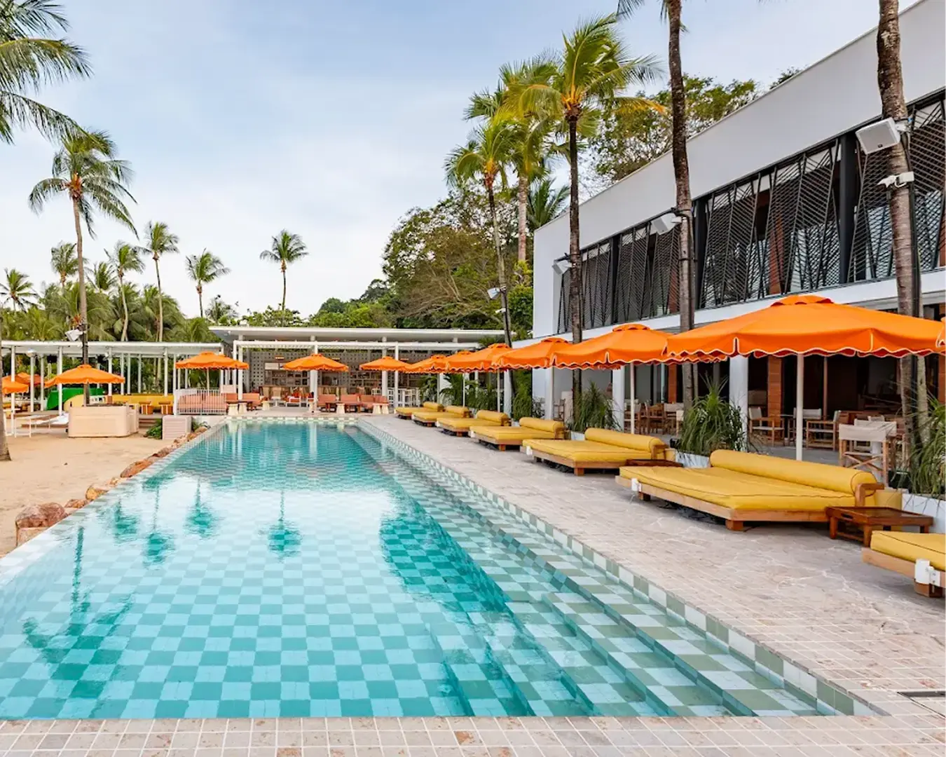 Sun lounger with an umbrella by the sparkling swimming pool at Tanjong Beach Club, a perfect spot to unwind and enjoy the tropical surroundings
