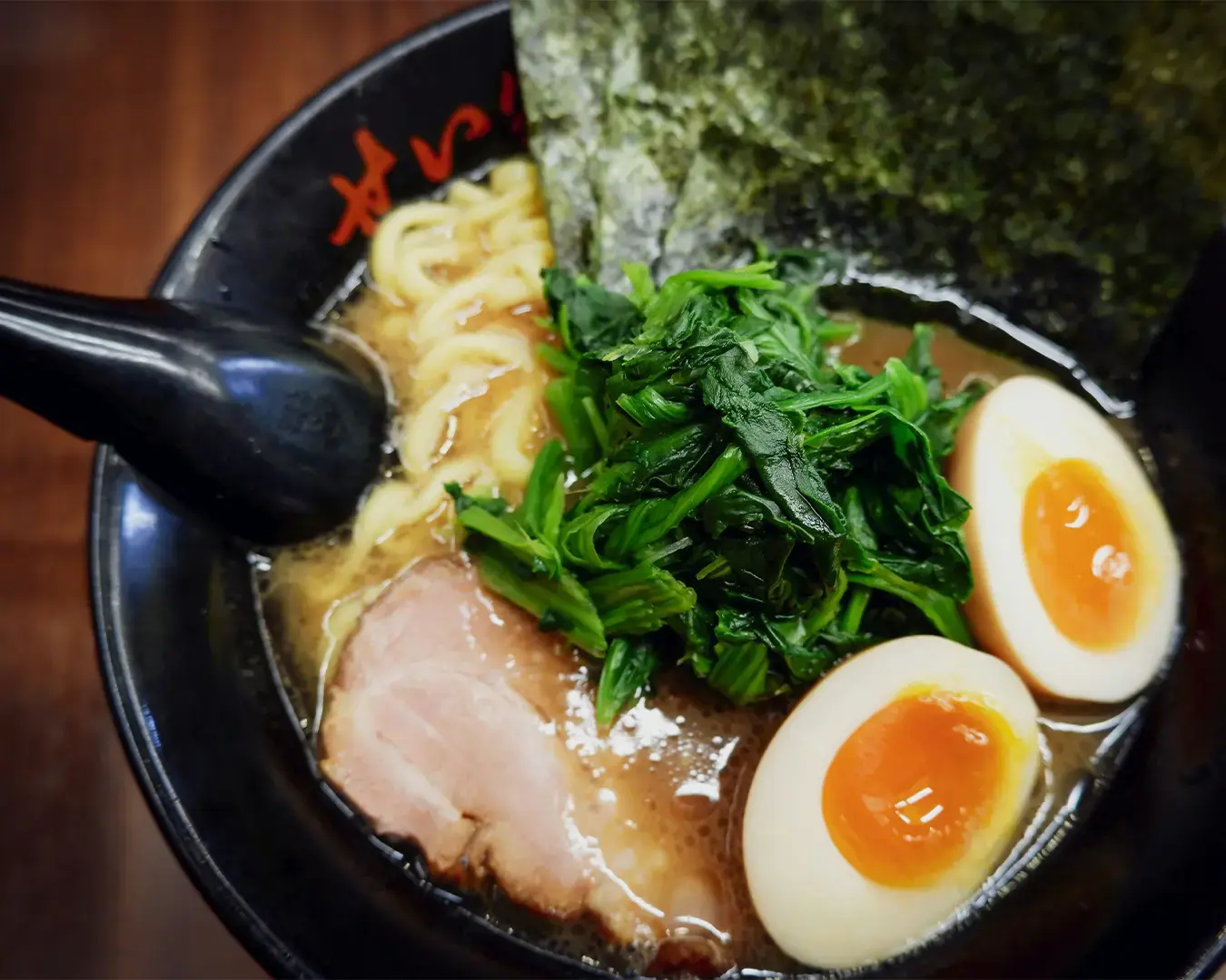 A bowl of ramen with creamy broth, topped with sliced pork, vibrant green spinach, two halved soft-boiled eggs, and a sheet of seaweed, exuding warmth.