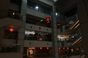 Low-angle interior shot of the multi-level atrium inside Cuppage Plaza, featuring dimly lit corridors, escalators, and glowing red paper lanterns suspended from the ceiling to highlight the mall's moody atmosphere.