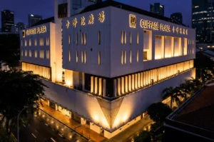 The exterior of Cuppage Plaza illuminated against the night sky, featuring a white facade, glowing vertical window slits, and prominent signage in both English and Chinese characters.