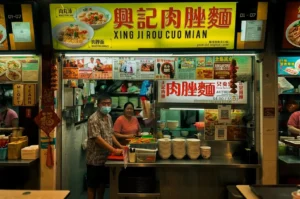 Xing Ji Ruo Cuo Mian store exterior with lighted signage and menu visible along with the vendors preparing Bak Chor Mee located at Bedok 85.