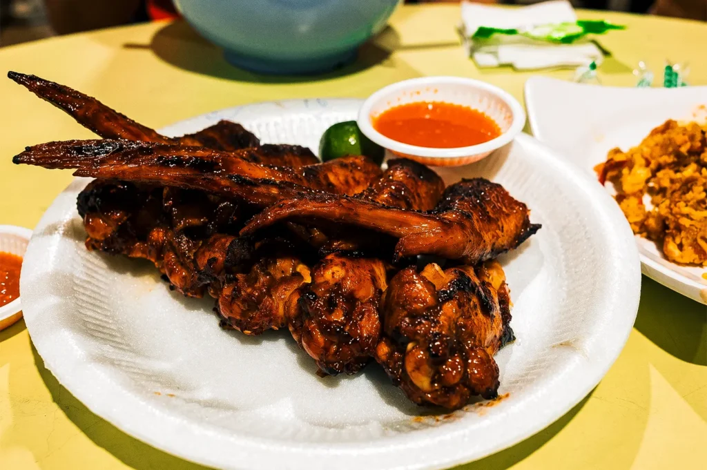 Chicken wings stacked on one another with lime and sauce on a white plate.