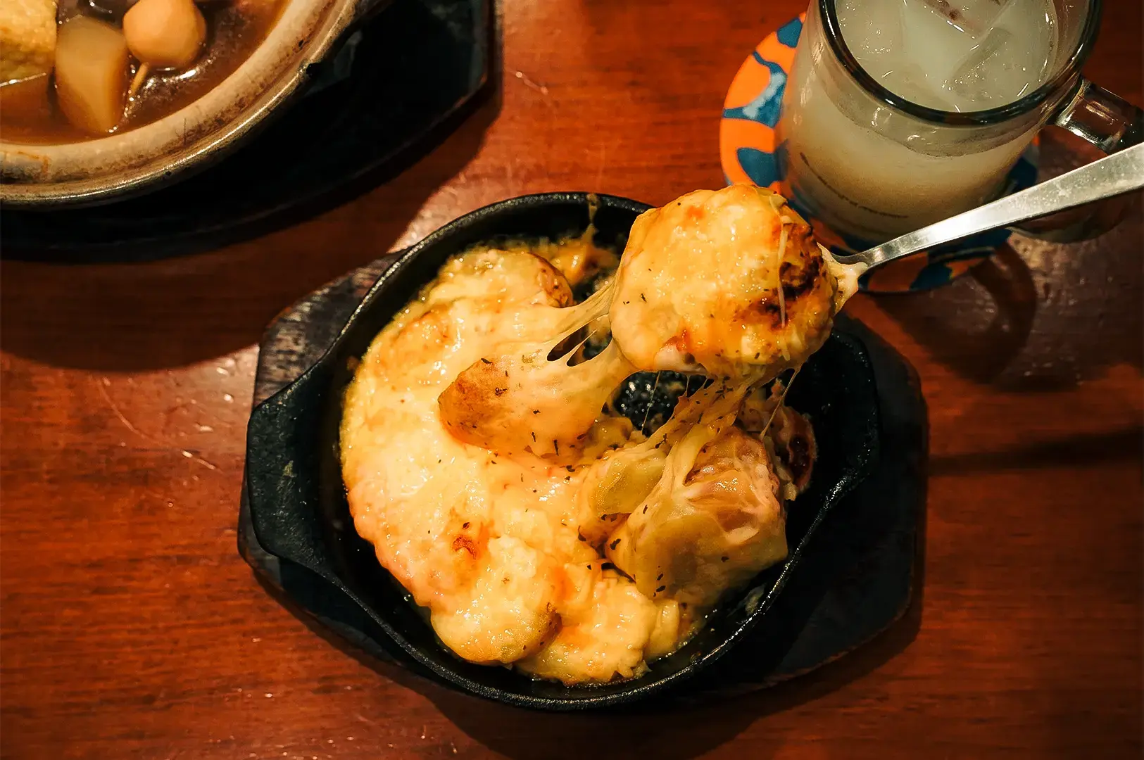 Keria Japanese Restaurant's Potato Cheese Mentai in a black bowl platter with a spoon taking a portion of the dish.