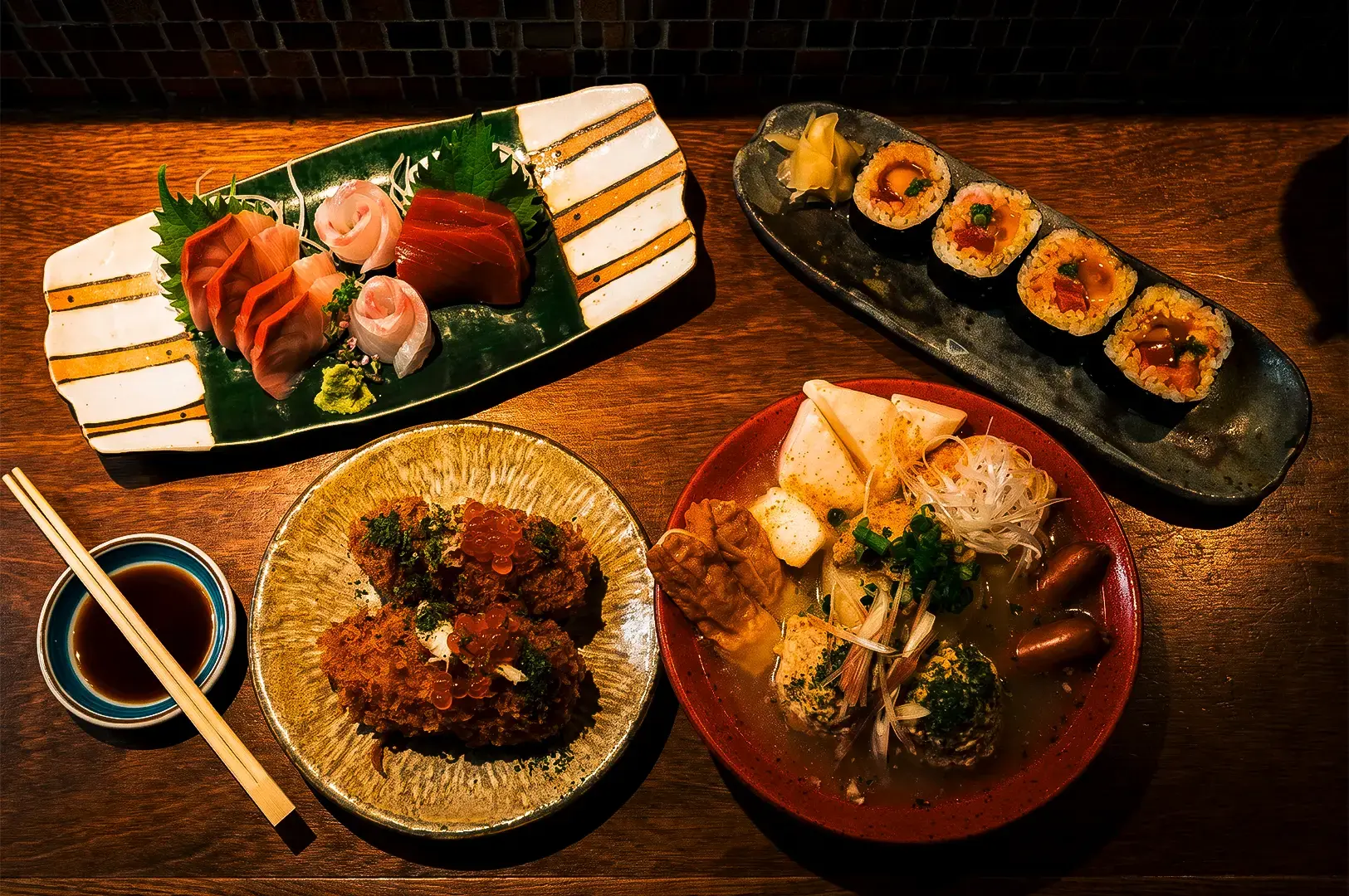 Apollon AM-Bar flat lay food shot including some of their famous dishes like Oden, Egg-Yolk Maki, and Crab Croquettes arranged on a wooden table illuminated by warm yellow light.