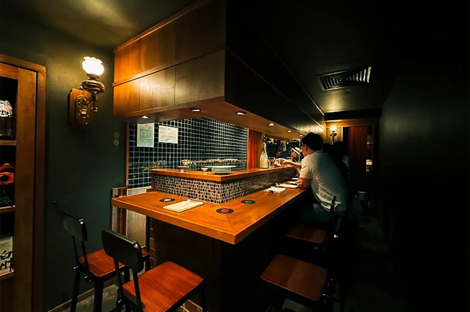 Apollon AM-Bar interior with a few customers sitting on the chair and long table, minimal lighting providing dim and cozy vibes.