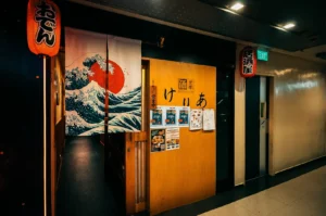 Keria Japanese Restaurant store exterior with its hanging cloth curtain showing a Japanese style graphic and red lanterns on either side of the wooden entrance.