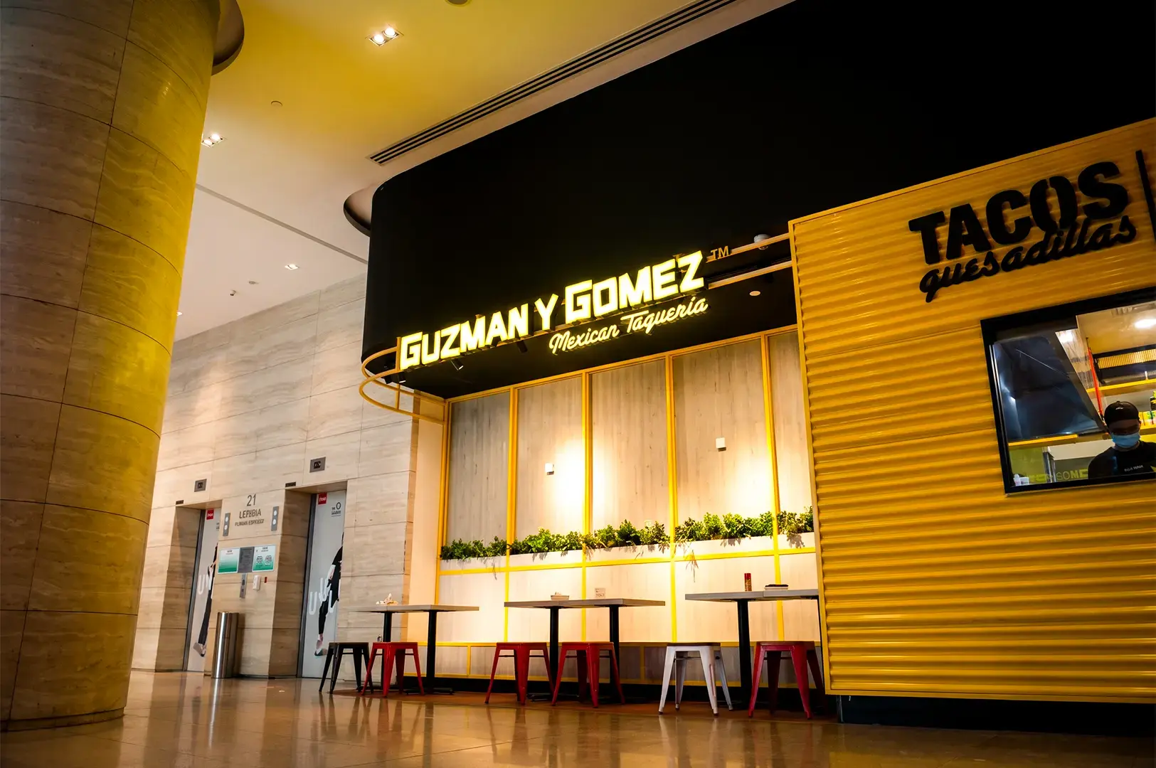 Guzman y Gomez Exterior dining area with its logo signage and ambient lights giving bright warm lighting in the area.