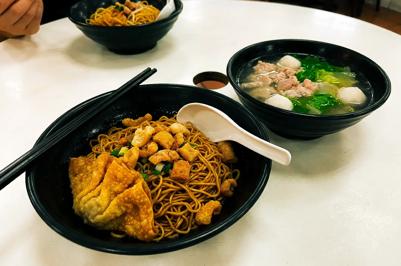 Two noodle bowls served on black bowls side by side each other on a white table served at XO Minced Meat Noodles at Newton Food Centre.