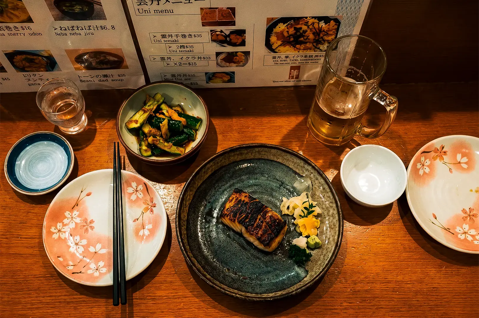Flat lay shot of Keria Japanese Restaurant fish dish on a black platter together with other plates and glasses on top of a wooden table.