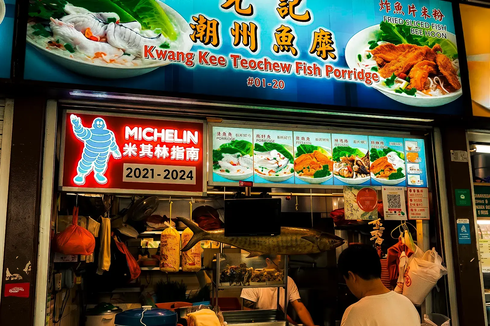 Kwang Kee Teochew Fish Porridge stall exterior with its logo signage and above and menu items hanging in front, fresh ingredients visible inside.