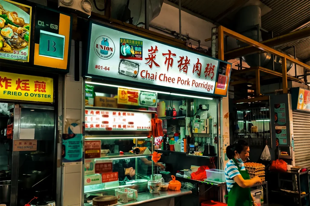 Chai Chee Pork Porridge stall exterior at Bedok 85 with its white and red backlit logo signage on top and their glass display and menu in front.
