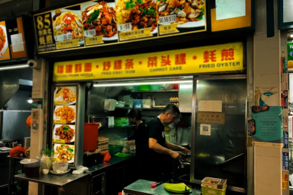 Bedok North Fried Oyster during night with busy staff cooking meals under their yellow logo signage and printed menu items.
