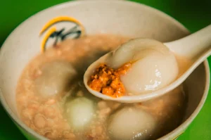A close up view of 75 Ah Balling Peanut Soup’s signature dish in a white bowl with a white spoon above holding a spoonful of the broth.