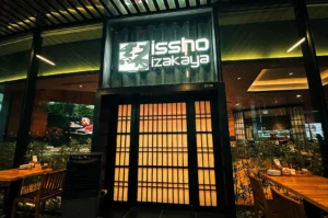 Issho Izakaya exterior with the logo signage on top of a traditional Japanese style entrance door with glass wall panels .
