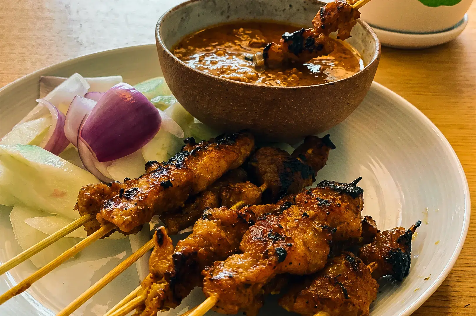 A closer view of barbecue skewers and dipping sauce with onions on a white plate served at Chong Pang Huat.