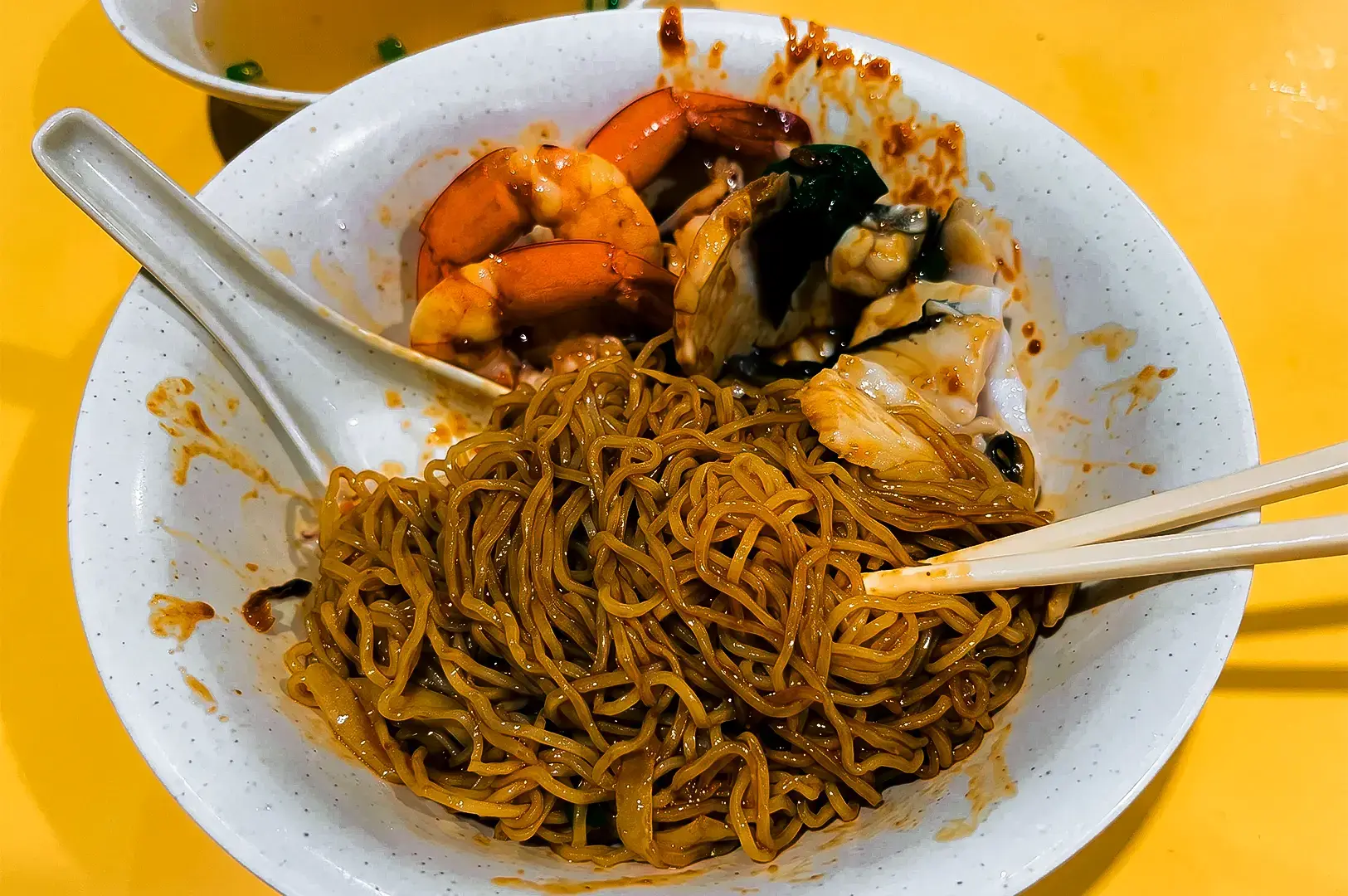 Dry noodles served at Hock Heng Fish Soup with its dark sauce coated noodles in a white bowl.