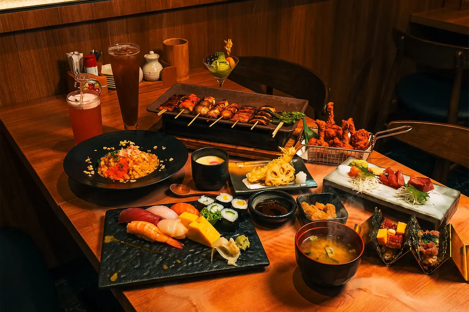 A variety of menu items served at Issho Izakaya on black and brown plates on a wooden table.