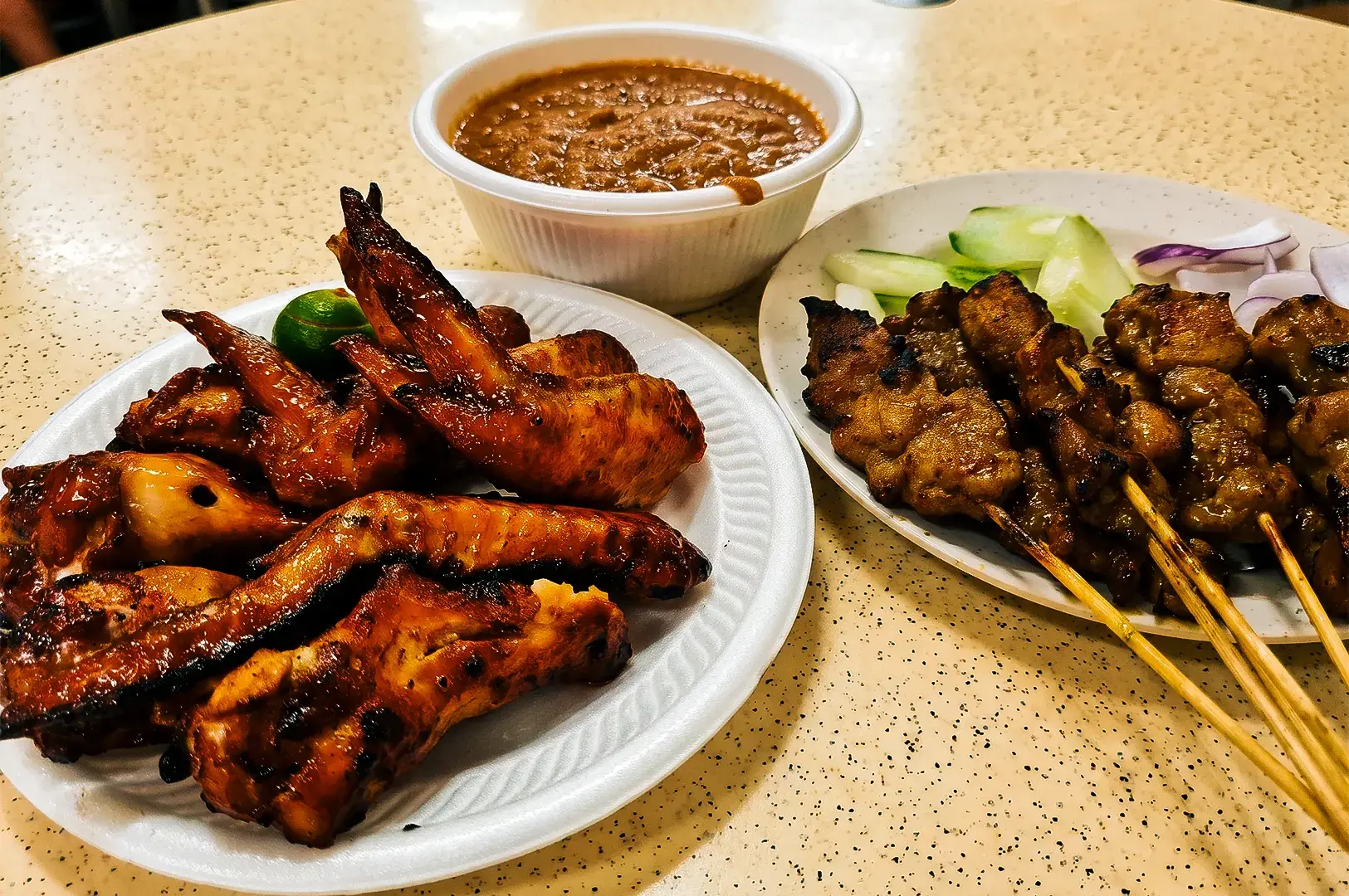 Barcecued chicken wings and satay served on paper plates and lime with dipping sauce at Chong Pang Huat.